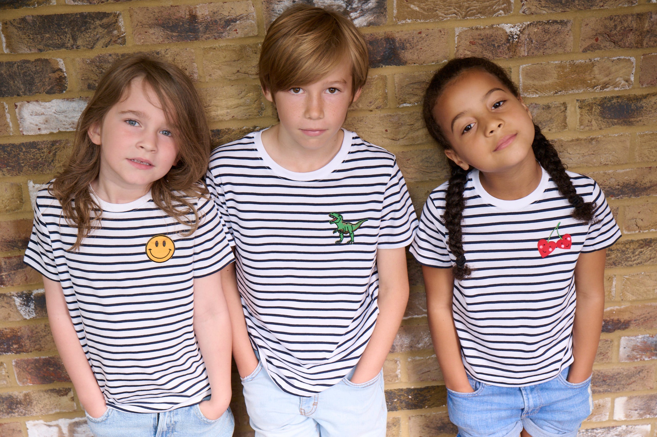 two boys and a girl wearing Breton stripe t-shirts standing against a brick wall