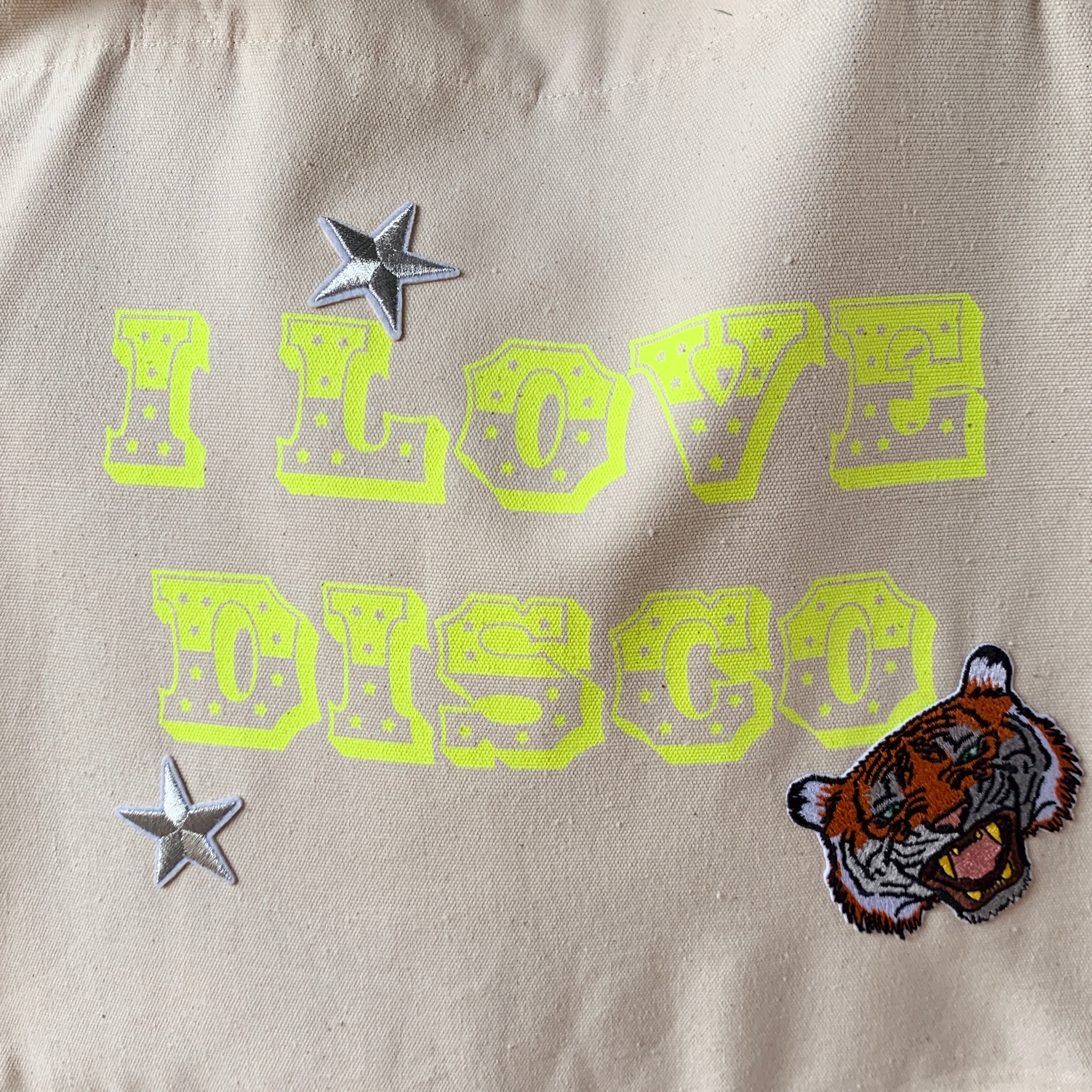 extra close up detail of neon yellow "I LOVE DISCO" print on cream tote bag with tiger iron on patch and 2 silver star iron on patches 